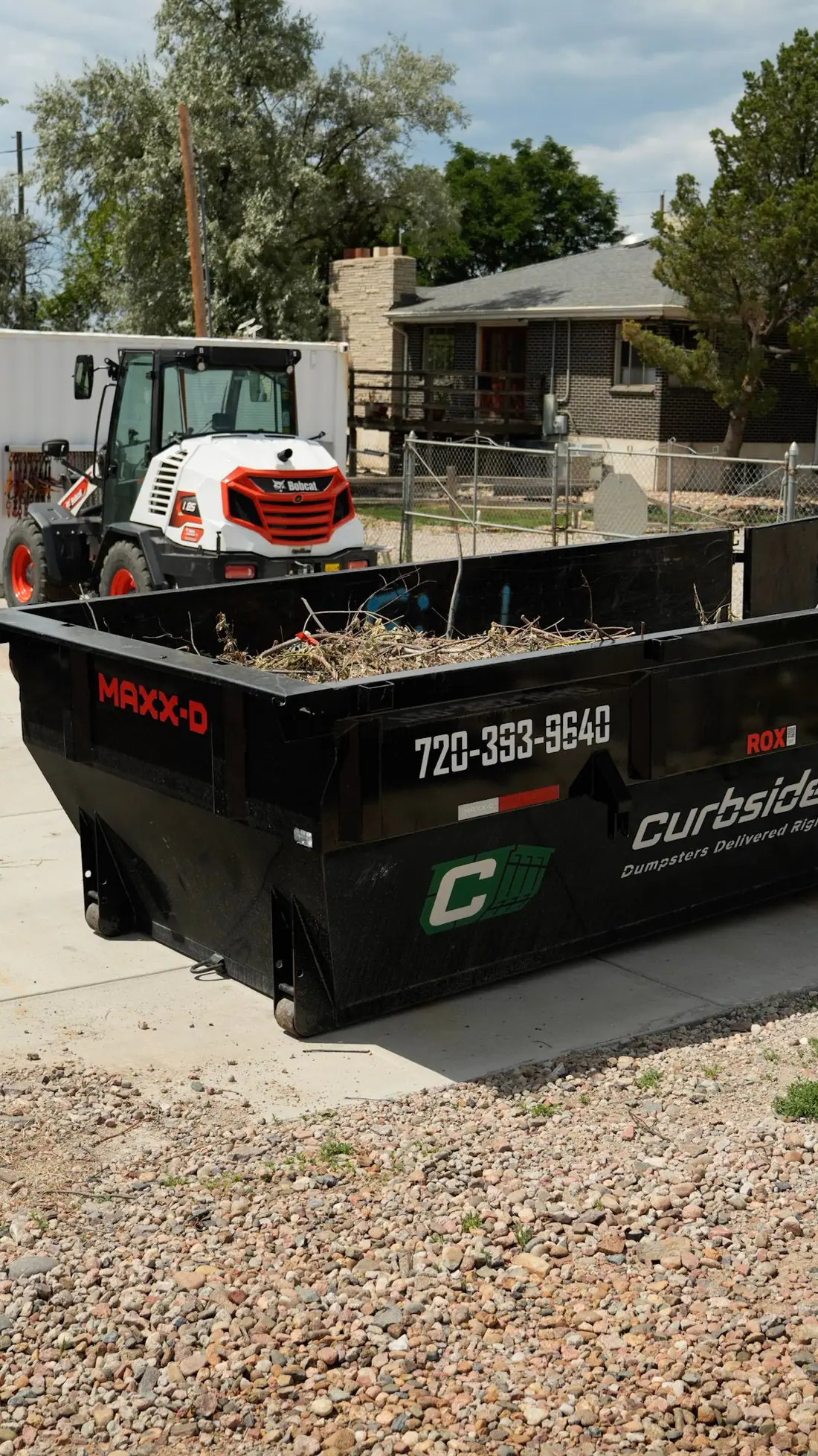 Roll-off dumpster loaded with yard waste next to a Bobcat loader